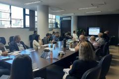 Sala de reuniões com integrantes do grupo de trabalho assistindo a uma apresentação