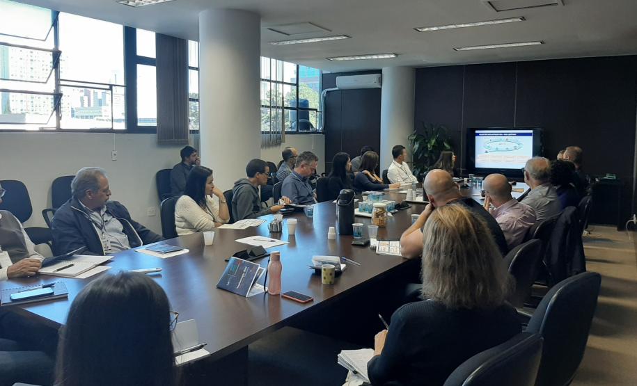 Sala de reuniões com integrantes do grupo de trabalho assistindo a uma apresentação